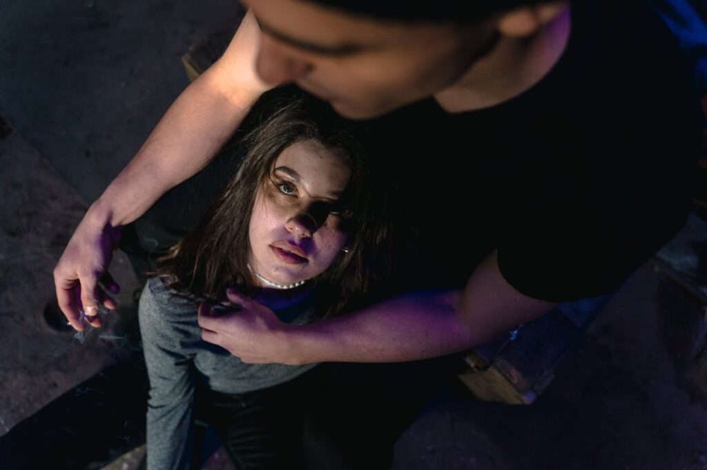 A man and woman seated closely in dim lighting, creating a moody atmosphere.